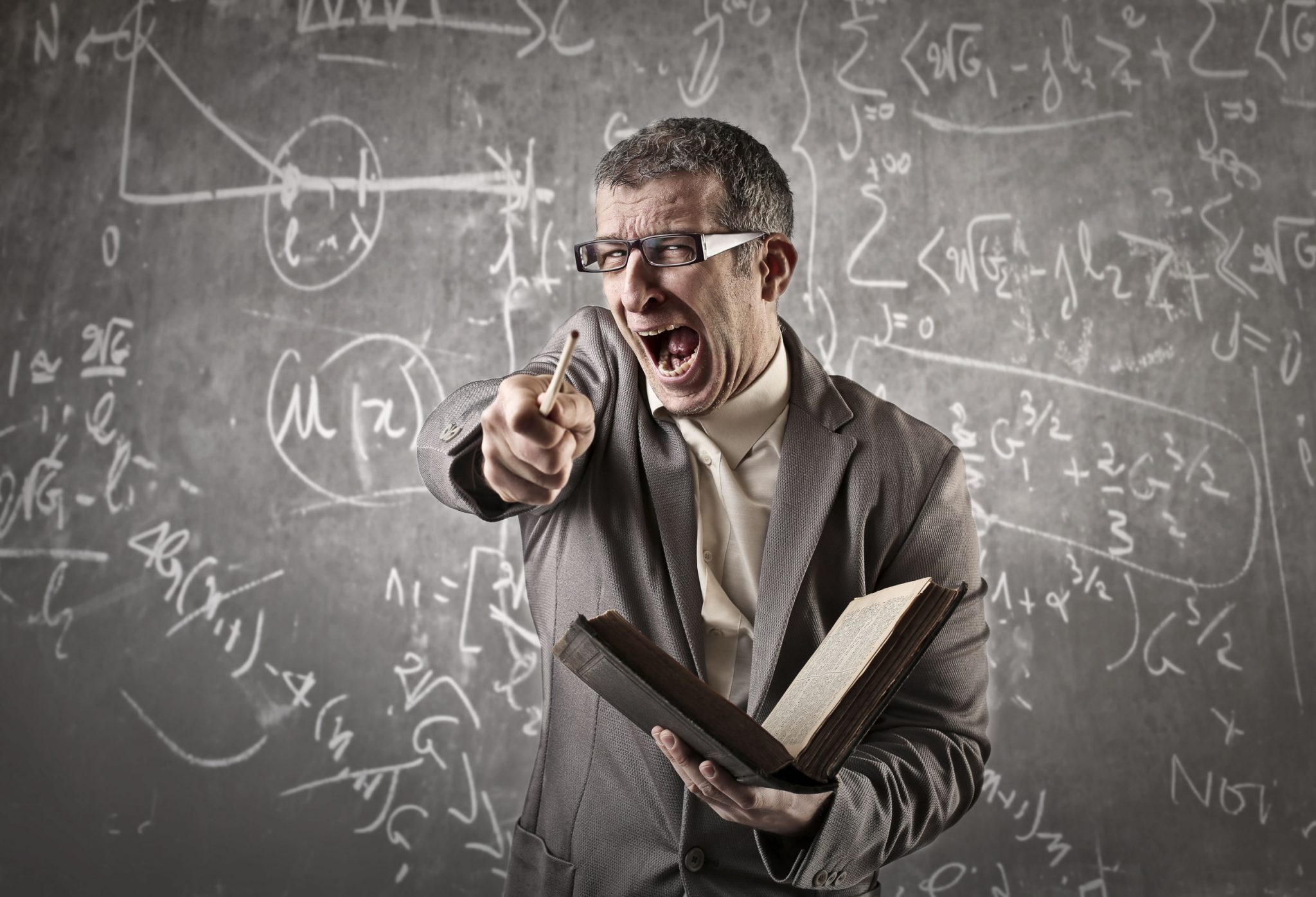 A teacher is shouting in a class room in front of a black board