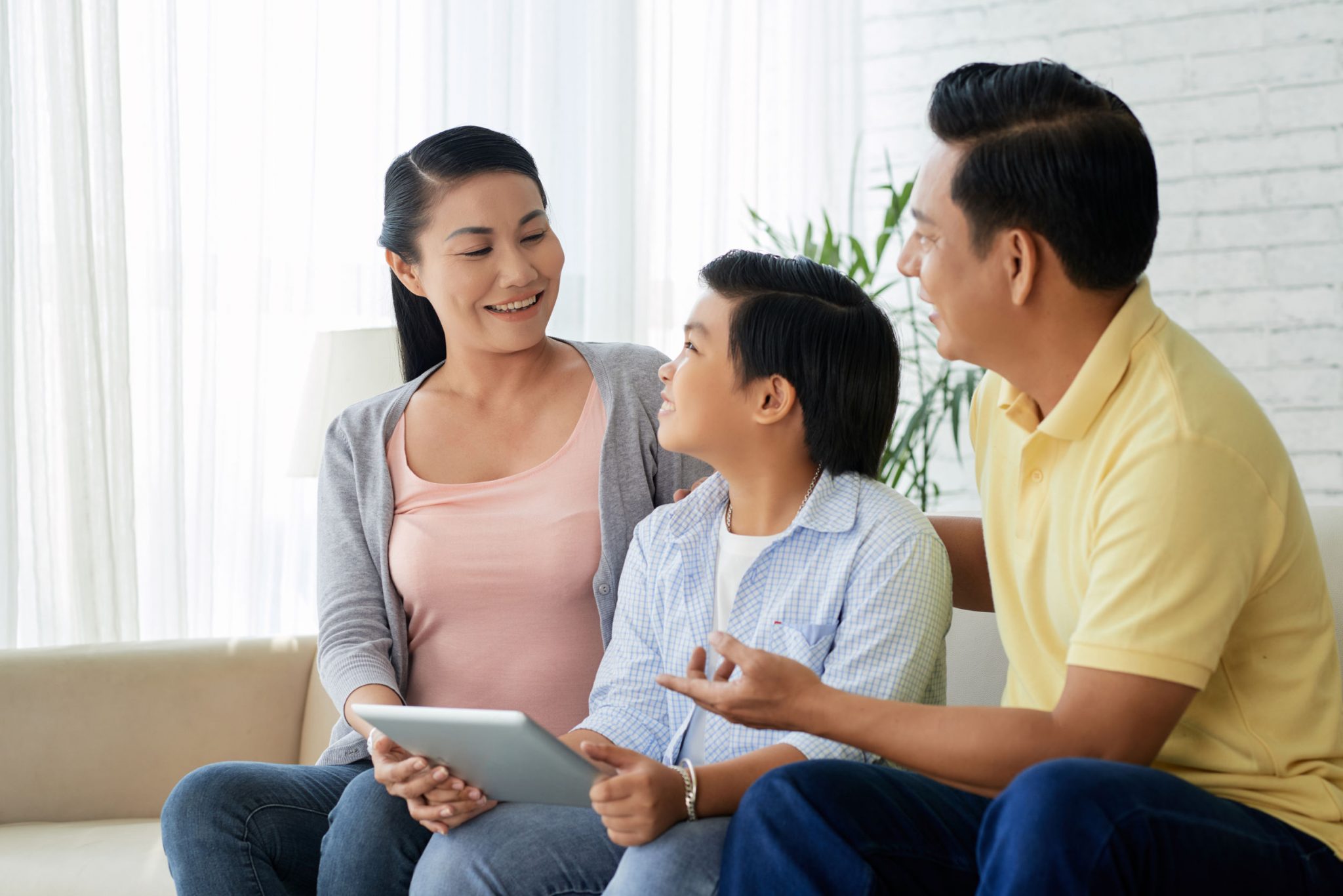 Happy parents spending their time with their child on sofa and the boy holding a tab in his hand