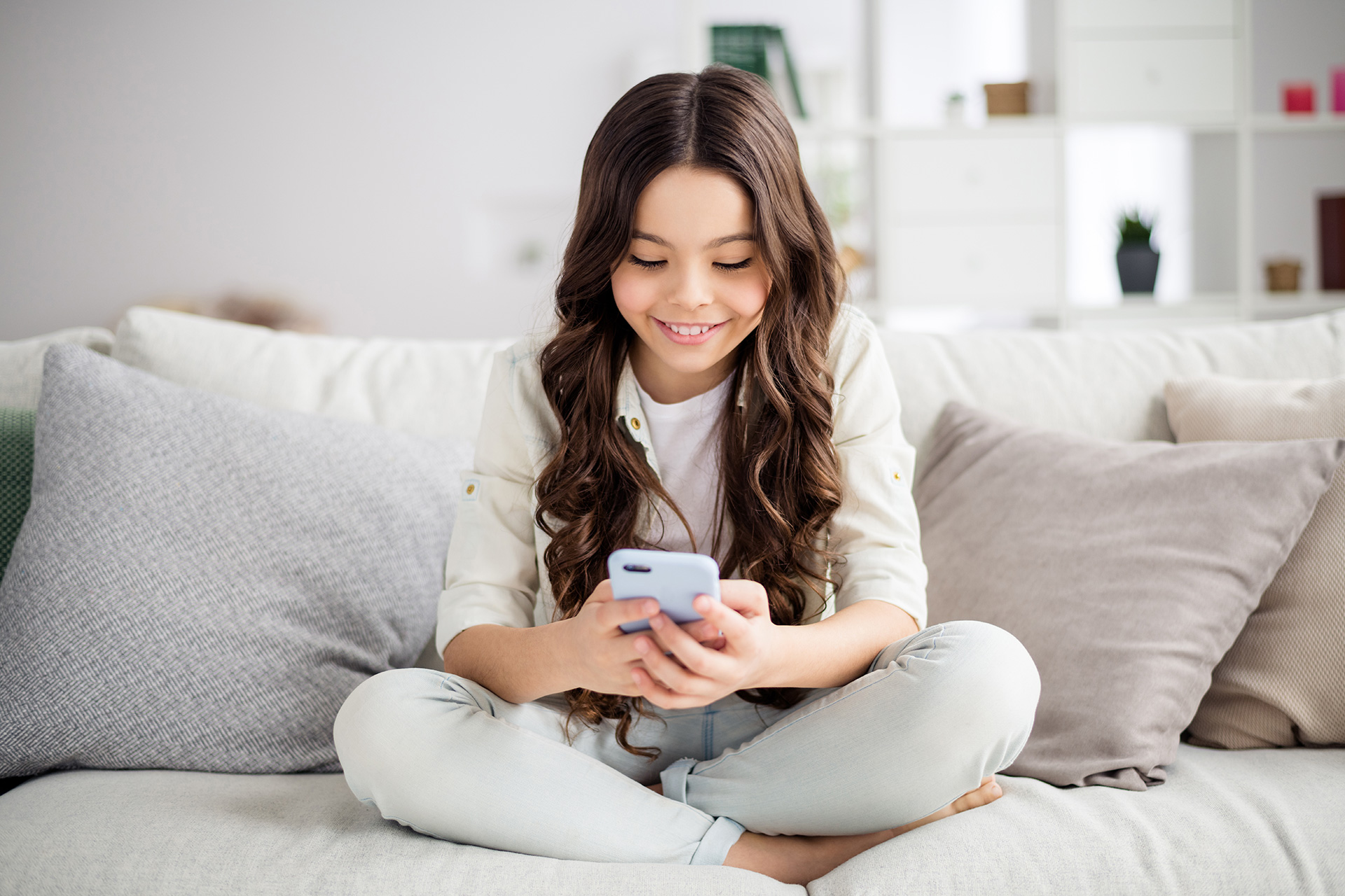 A happy girl using phone at home sitting on the sofa