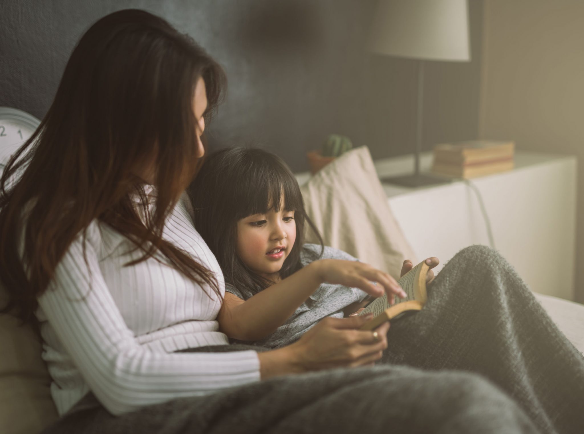 A mother showing something to her baby girl on her phone screen in bed time