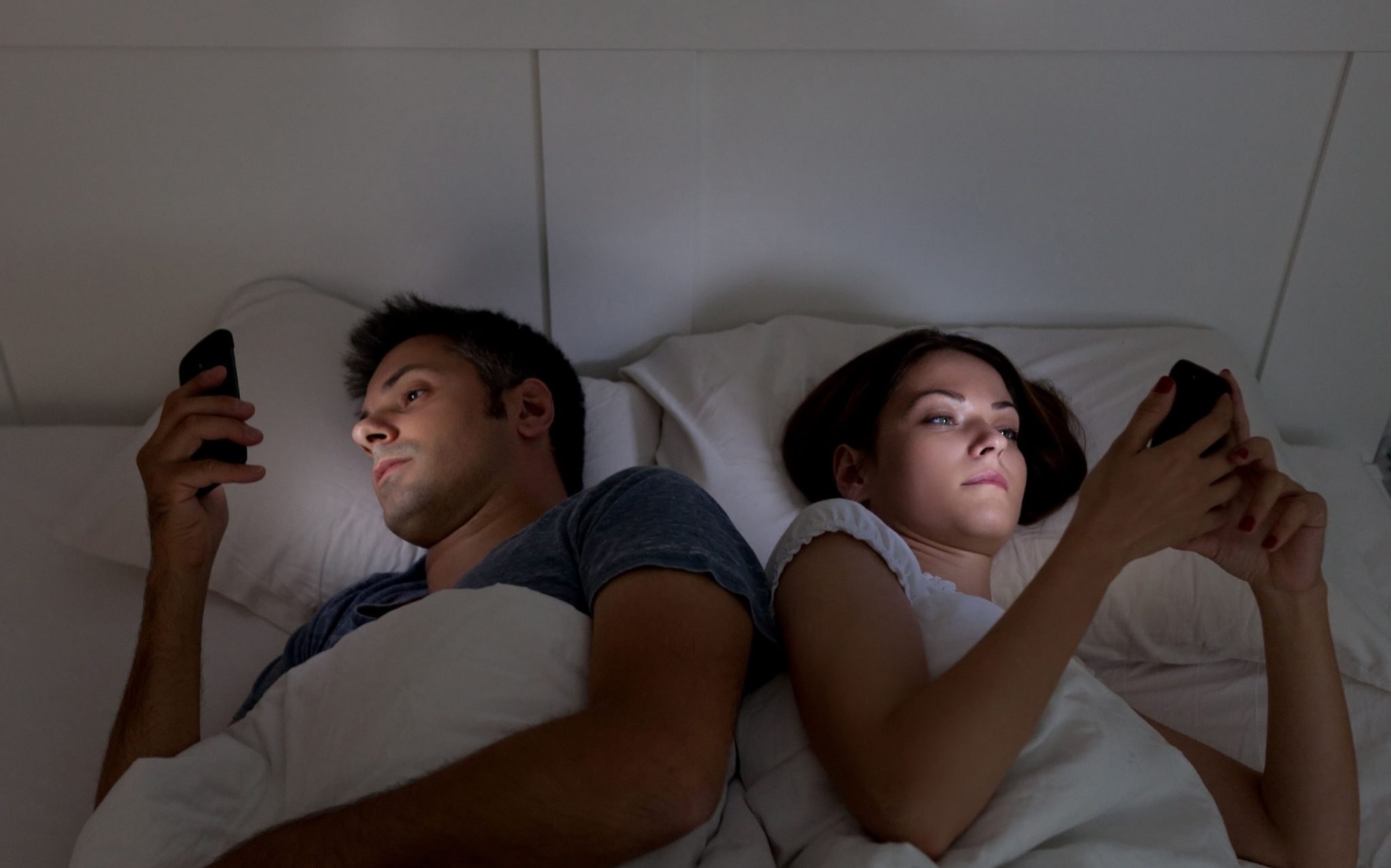 A couple using there phone in their bed at midnight